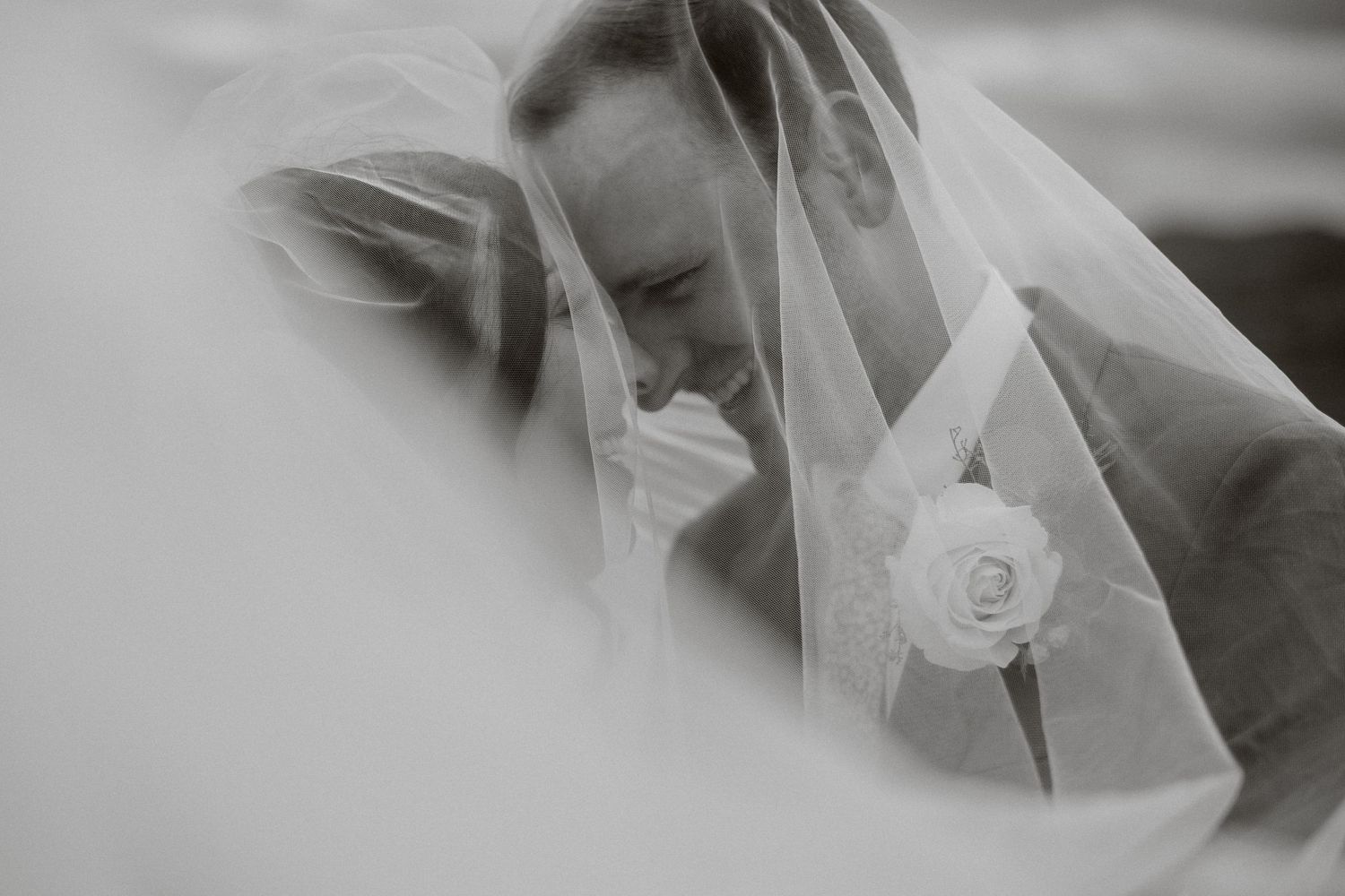 A black and white close up photograph of a bride wearing a delicate veil with a rose details.