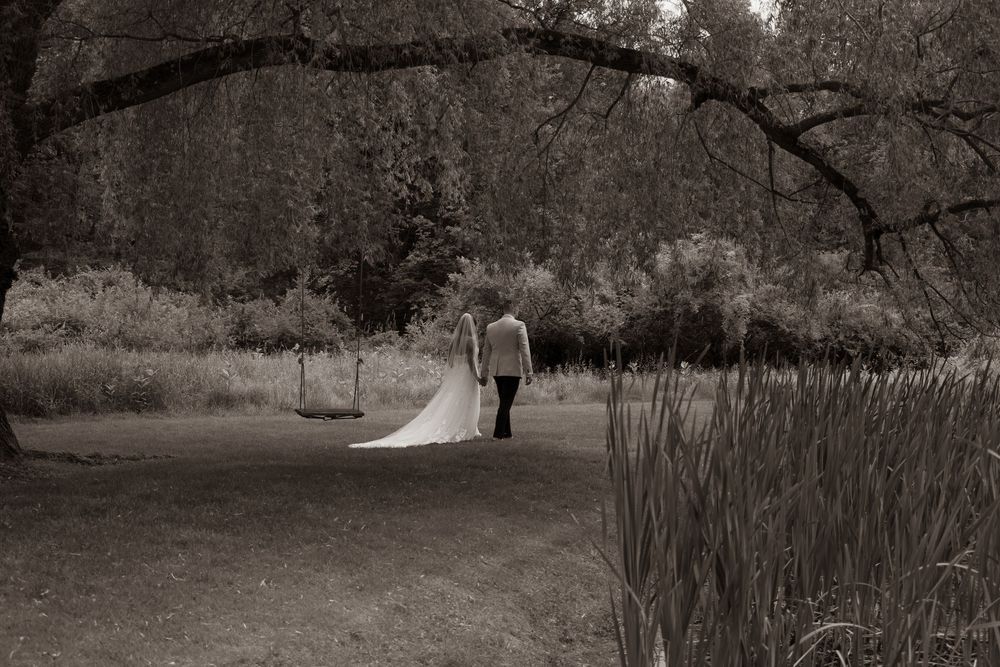 A couple walking down a garden path under an arching tree branch in black and white photography.