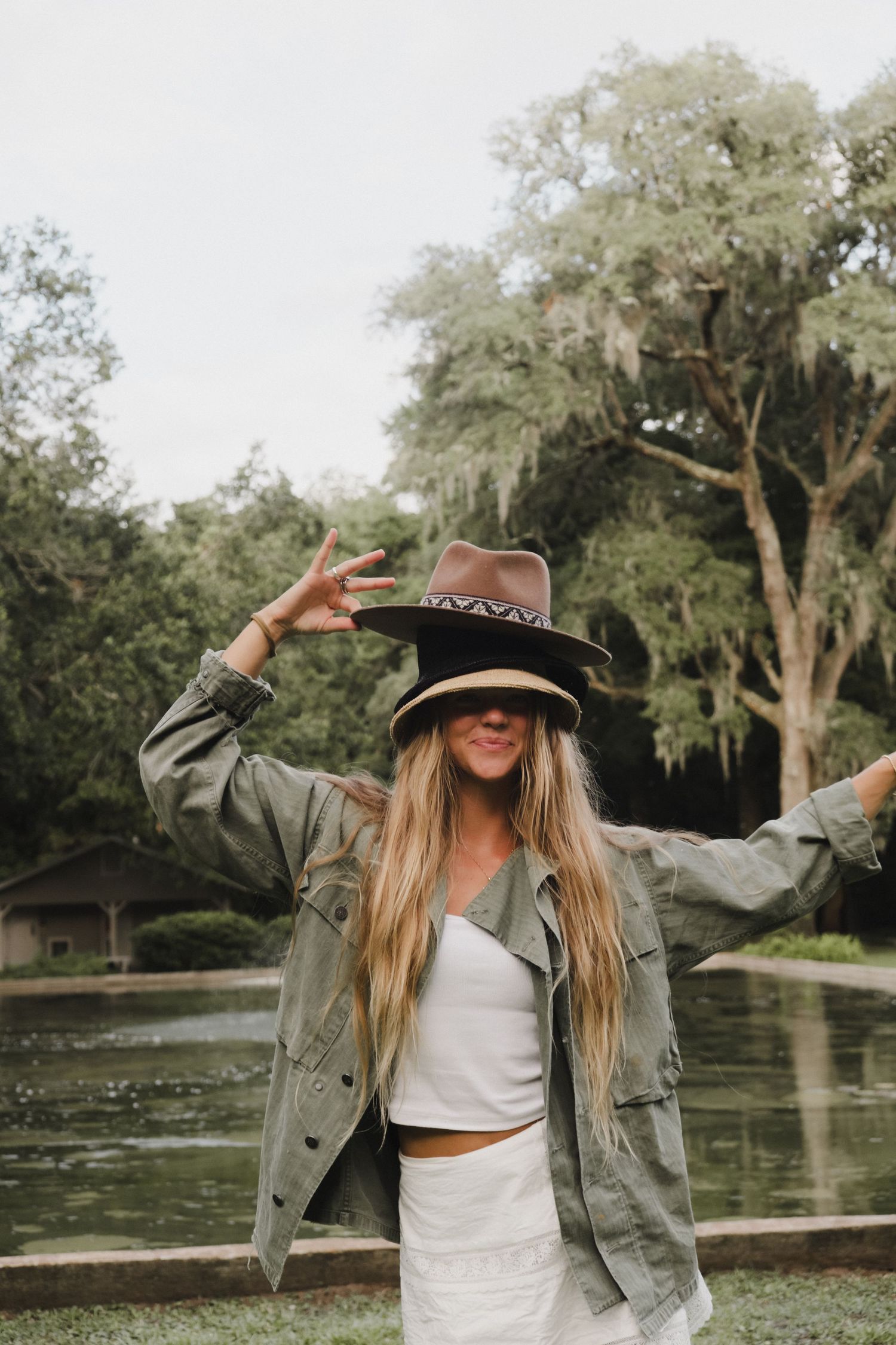 Figure in military jacket and hat dancing playfully by a pond with Spanish moss trees.