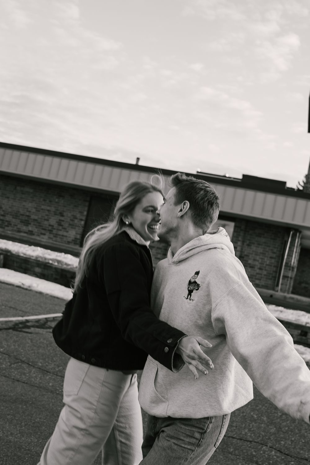 Black and white photo of a happy couple embracing and laughing together outdoors in winter.