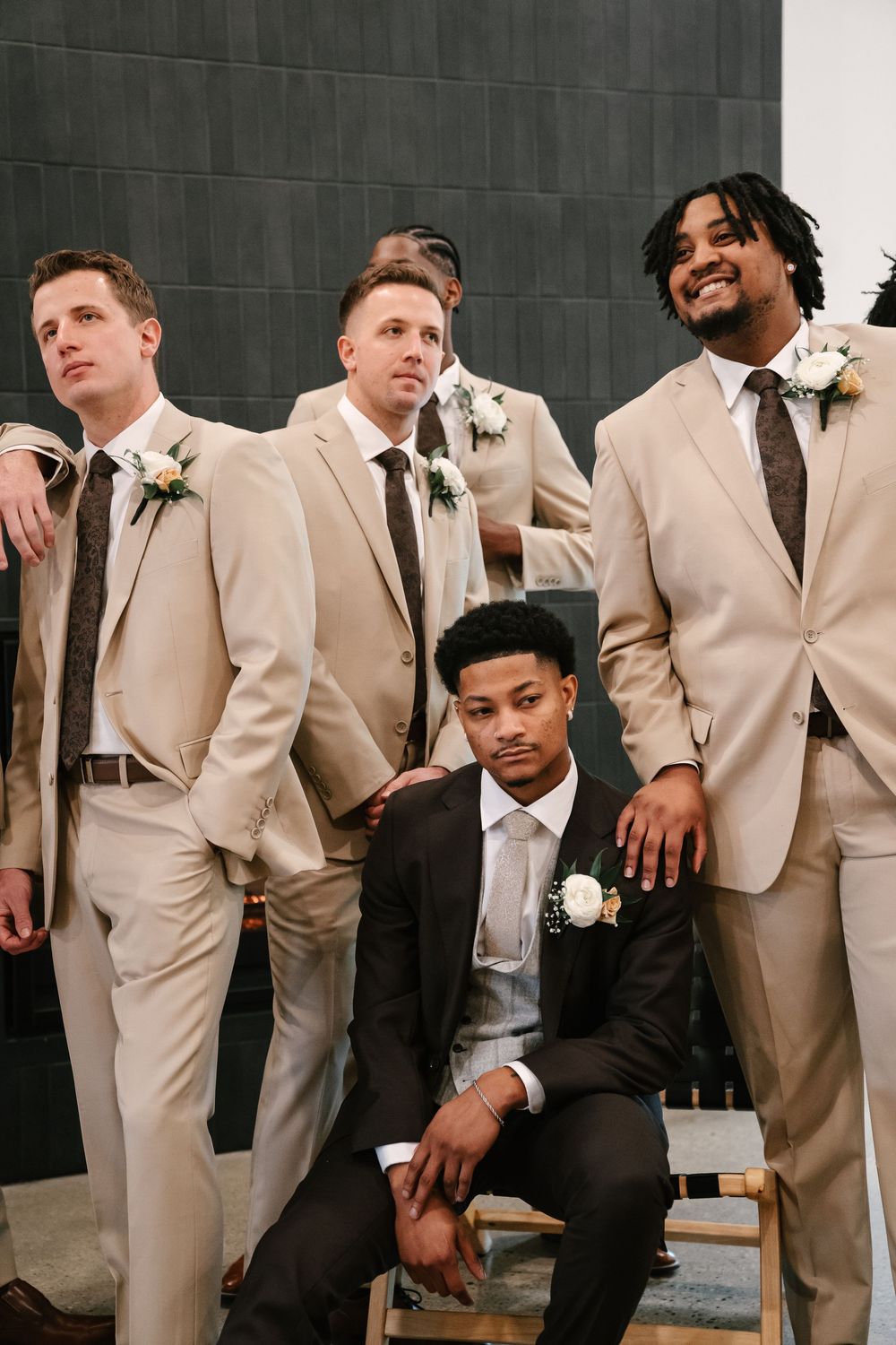 Diverse groomsmen in beige suits with boutonnieres pose together at a wedding ceremony.