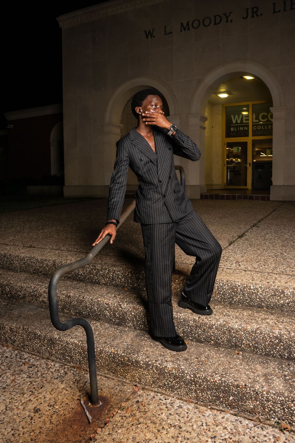 Person in pinstripe suit posing on steps outside W.L. Moody Jr. building at night.