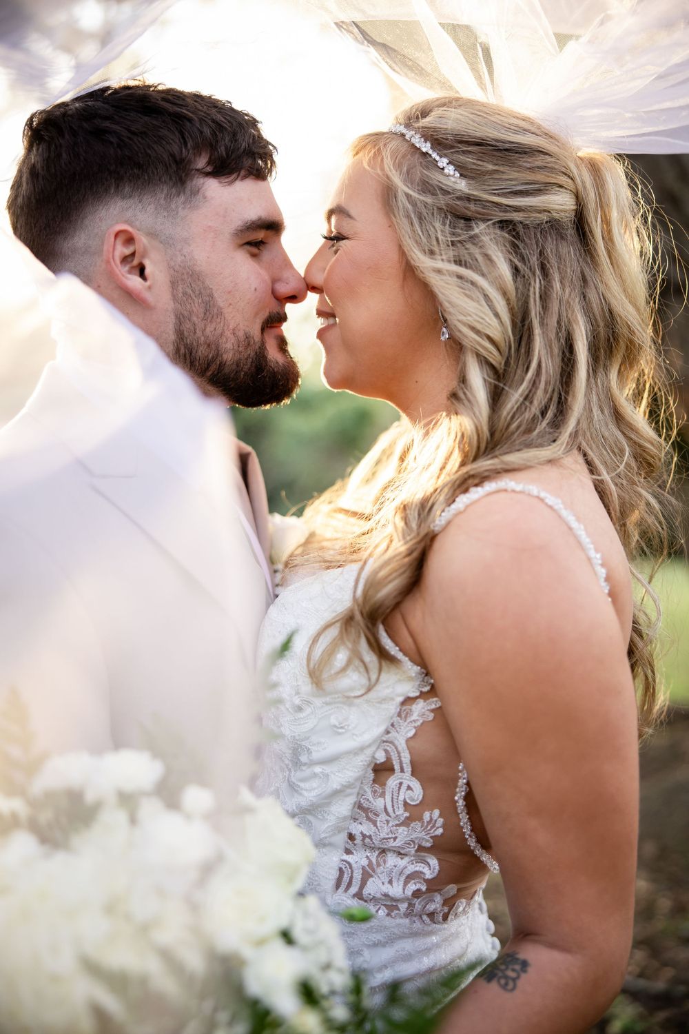 A romantic wedding moment captured between two people sharing a tender kiss under a flowing veil in natural lighting.