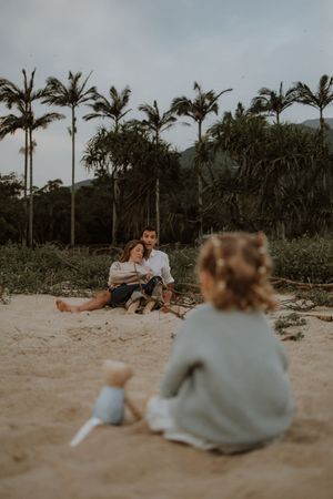 A couple sits together on a tropical beach with palm trees at sunset, creating a romantic silhouette against the sand.