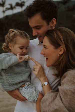 A family shares a tender moment together outdoors during golden hour, smiling and embracing in casual sweaters.