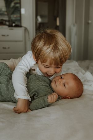 A series of tender moments showing a young child in a white shirt kissing a sleeping baby on a bed.