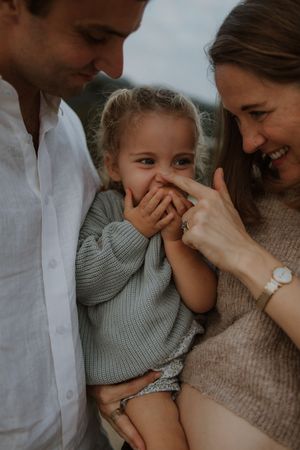 A happy family shares a tender moment together, with a child giggling between parents in soft lighting.
