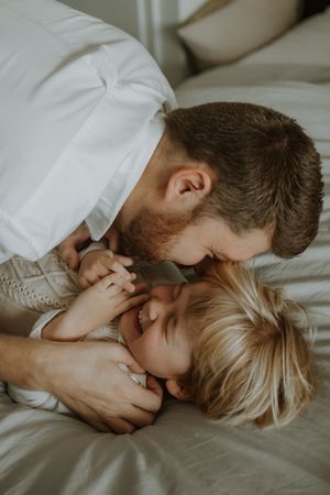 A tender moment of affection shared between two people lying on white bedding in soft natural light.