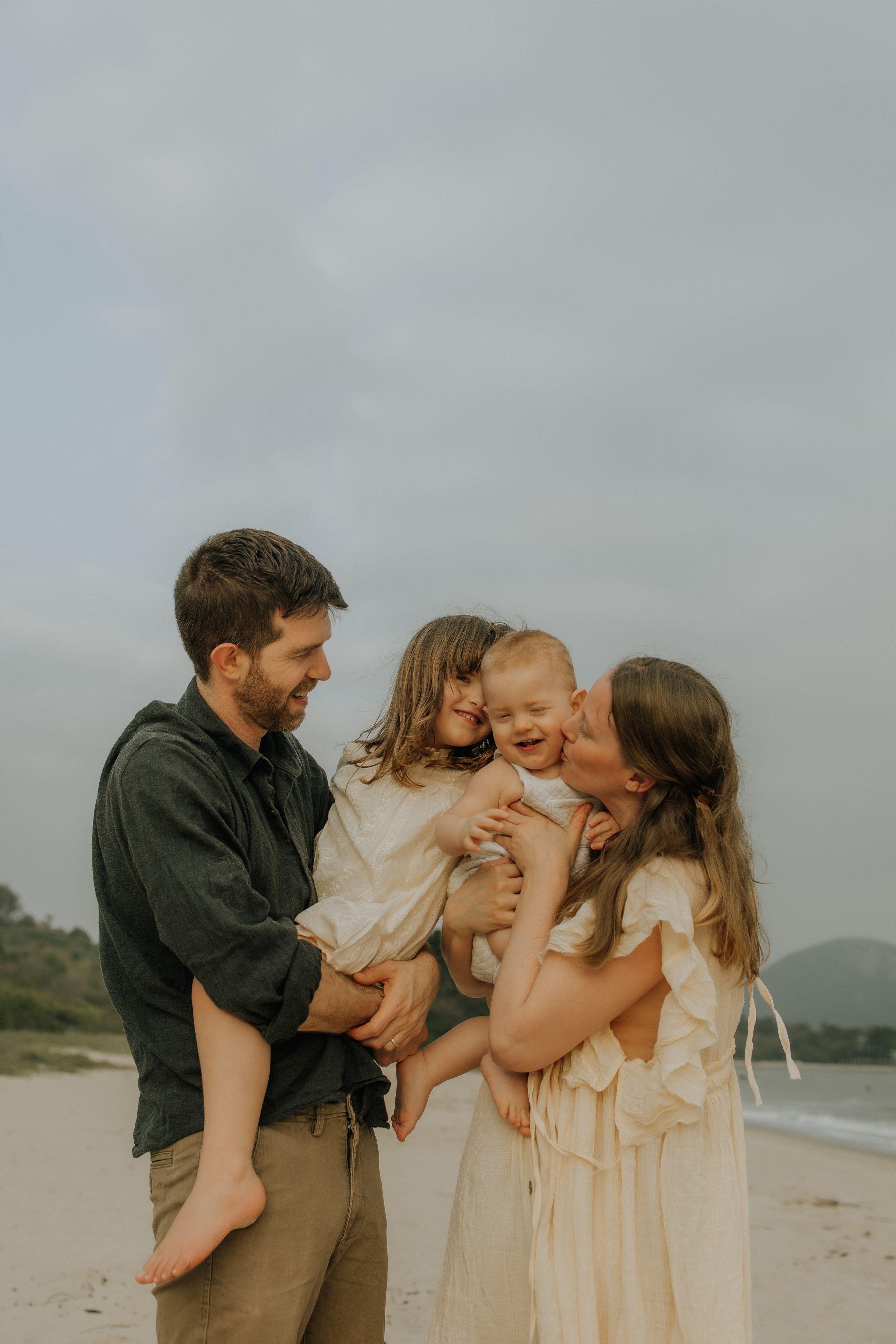 A family shares tender moments together on a misty beach in neutral colored outfits.