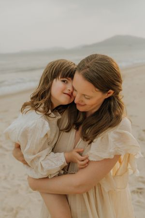 A tender moment shared between two people in white dresses on a beach with soft lighting and mountains in the background.