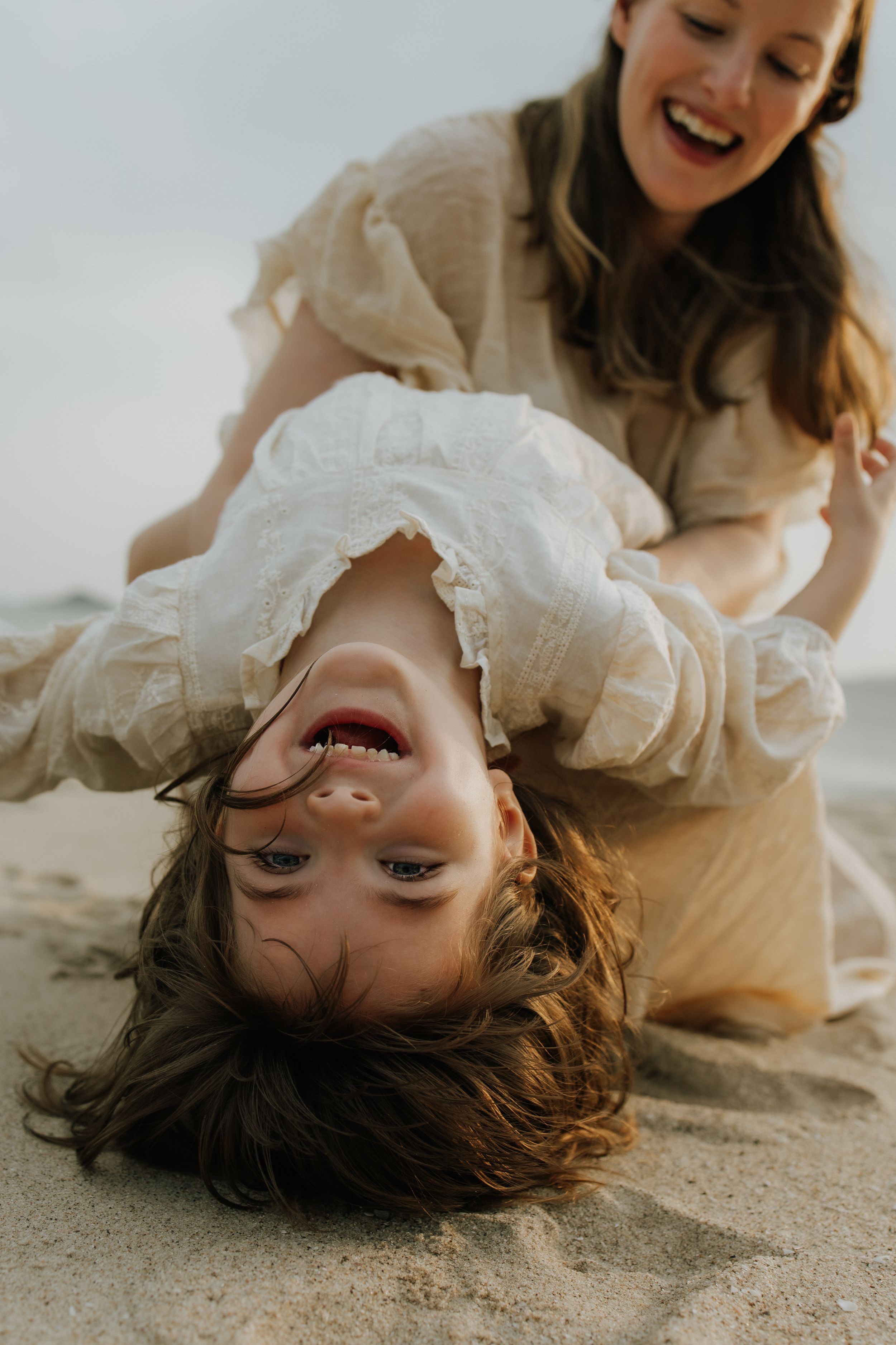 Playful beach portraits showing joyful expressions while laying in the sand with light colored dresses.