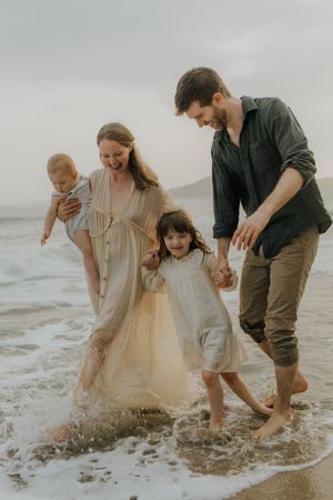A family plays together in the ocean waves at the beach on an overcast day, splashing in the shallow water.