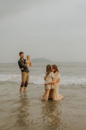 A family plays together in the shallow ocean waves on an overcast day at the beach.