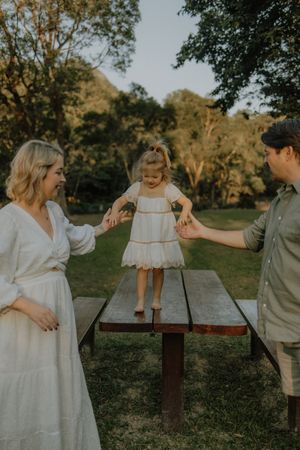 A couple and a small child share tender moments at a rustic picnic table during golden hour in a park setting.