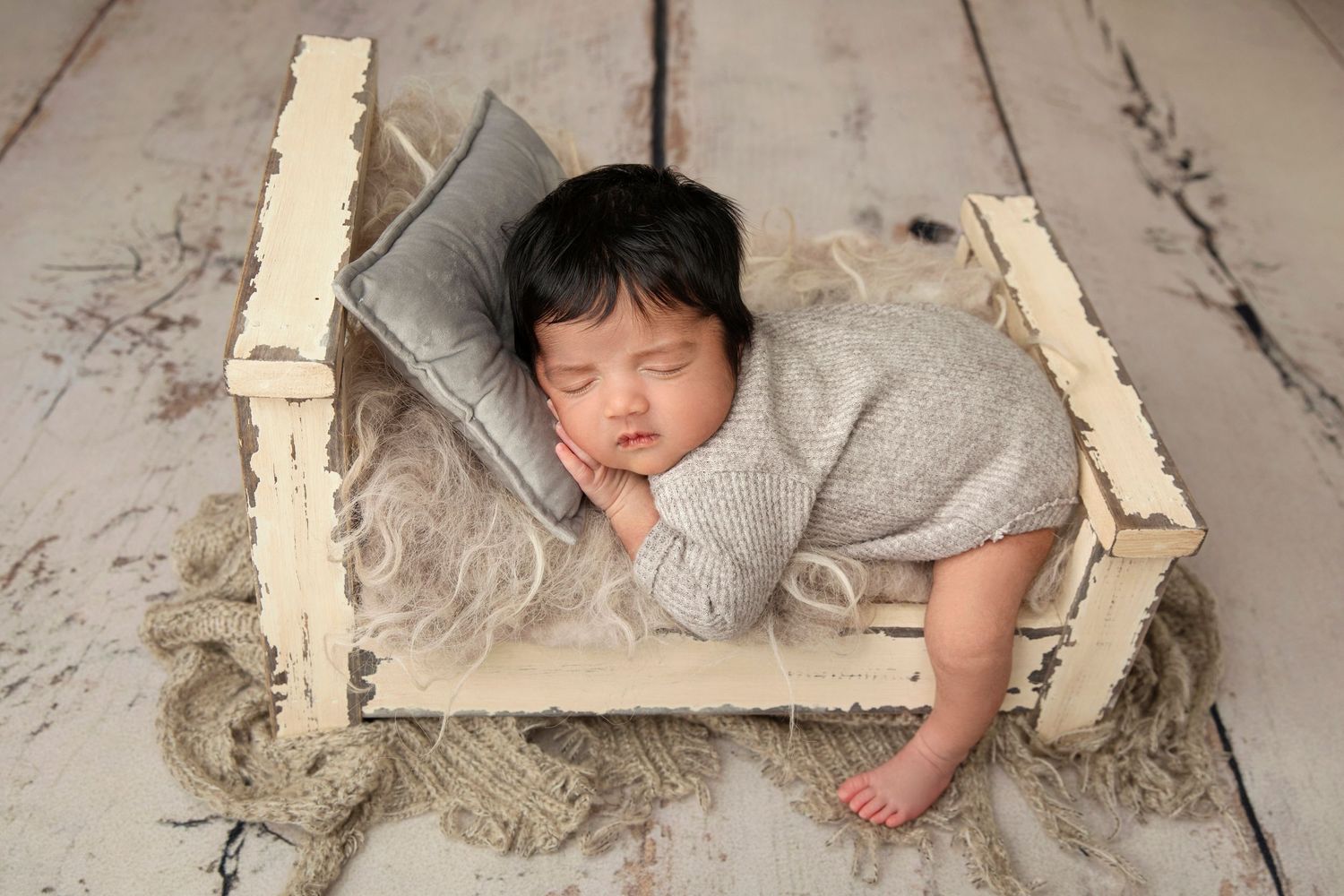 Sleeping baby rests on rustic wooden crate against white wooden floor background.