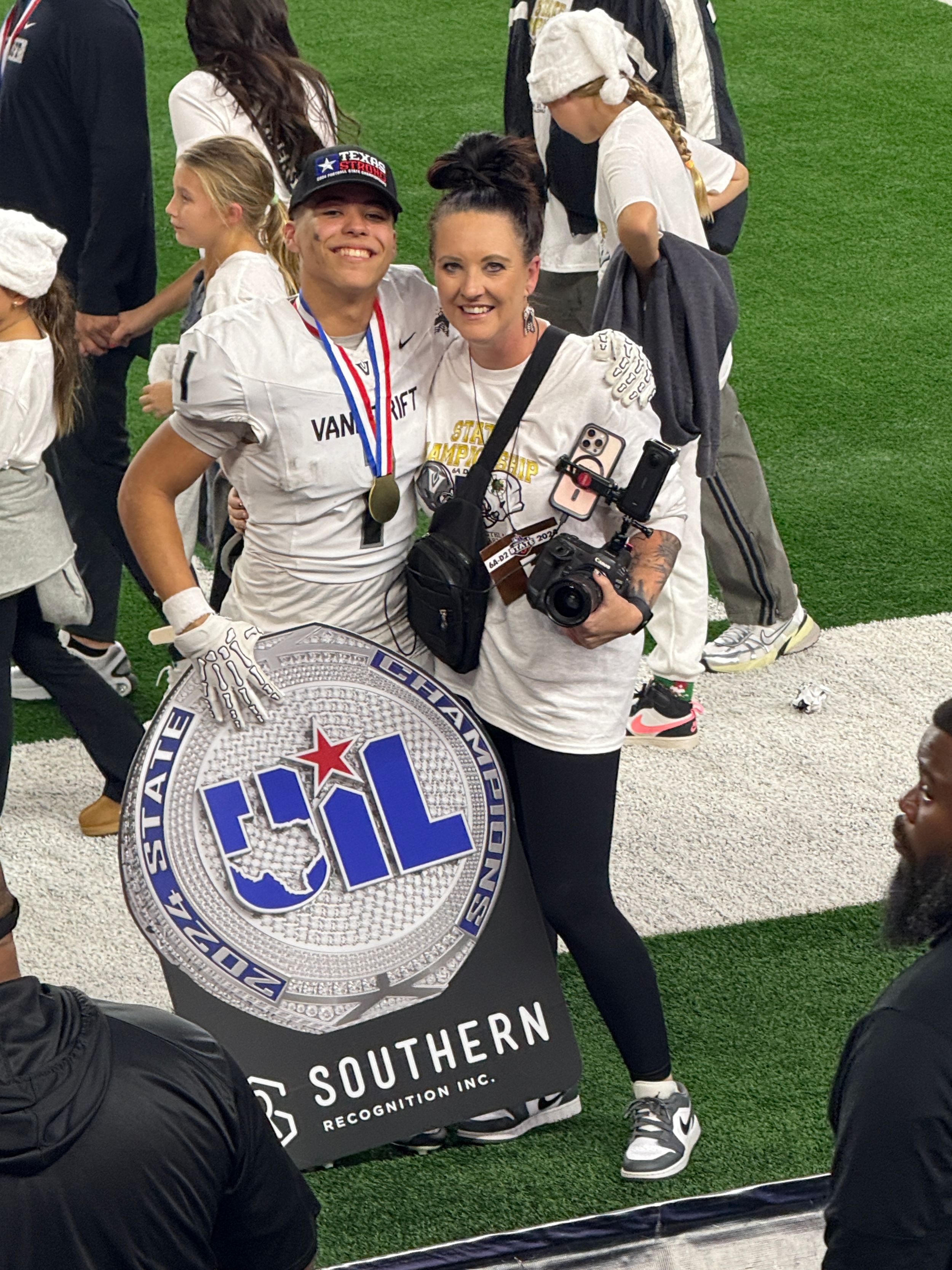 Photographer with cameras and football player posing next to UIL sports competition logo sign.