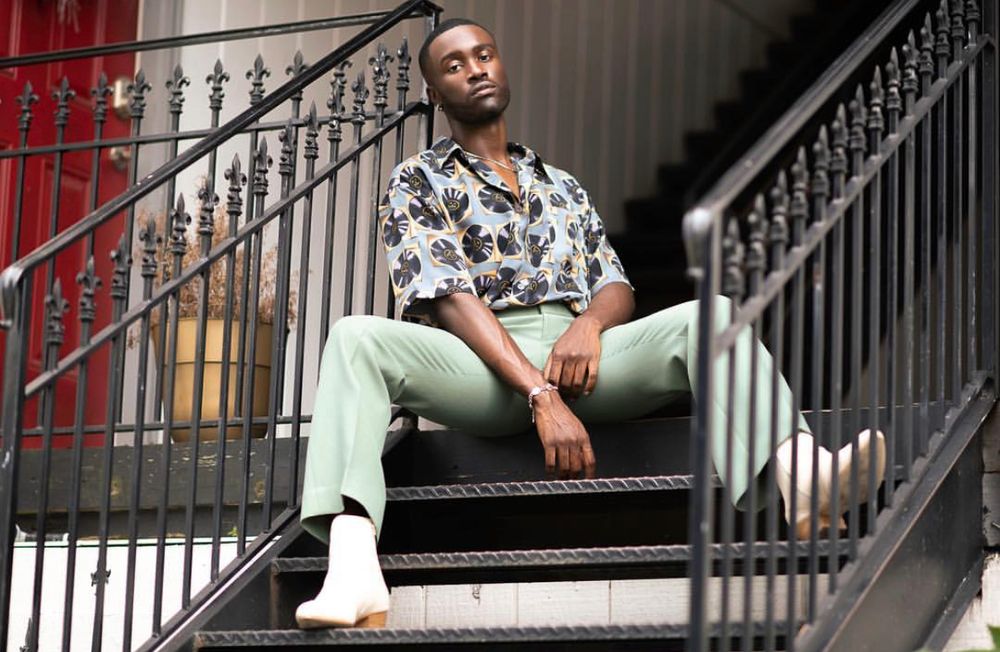 Man sitting on staircase wearing floral print shirt and mint green pants with white shoes.