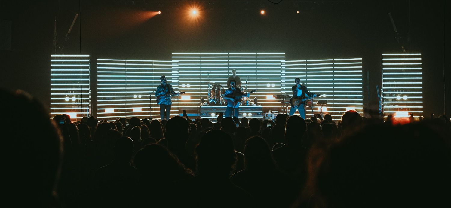 Concert stage with backlit performers silhouetted against striped LED light display.
