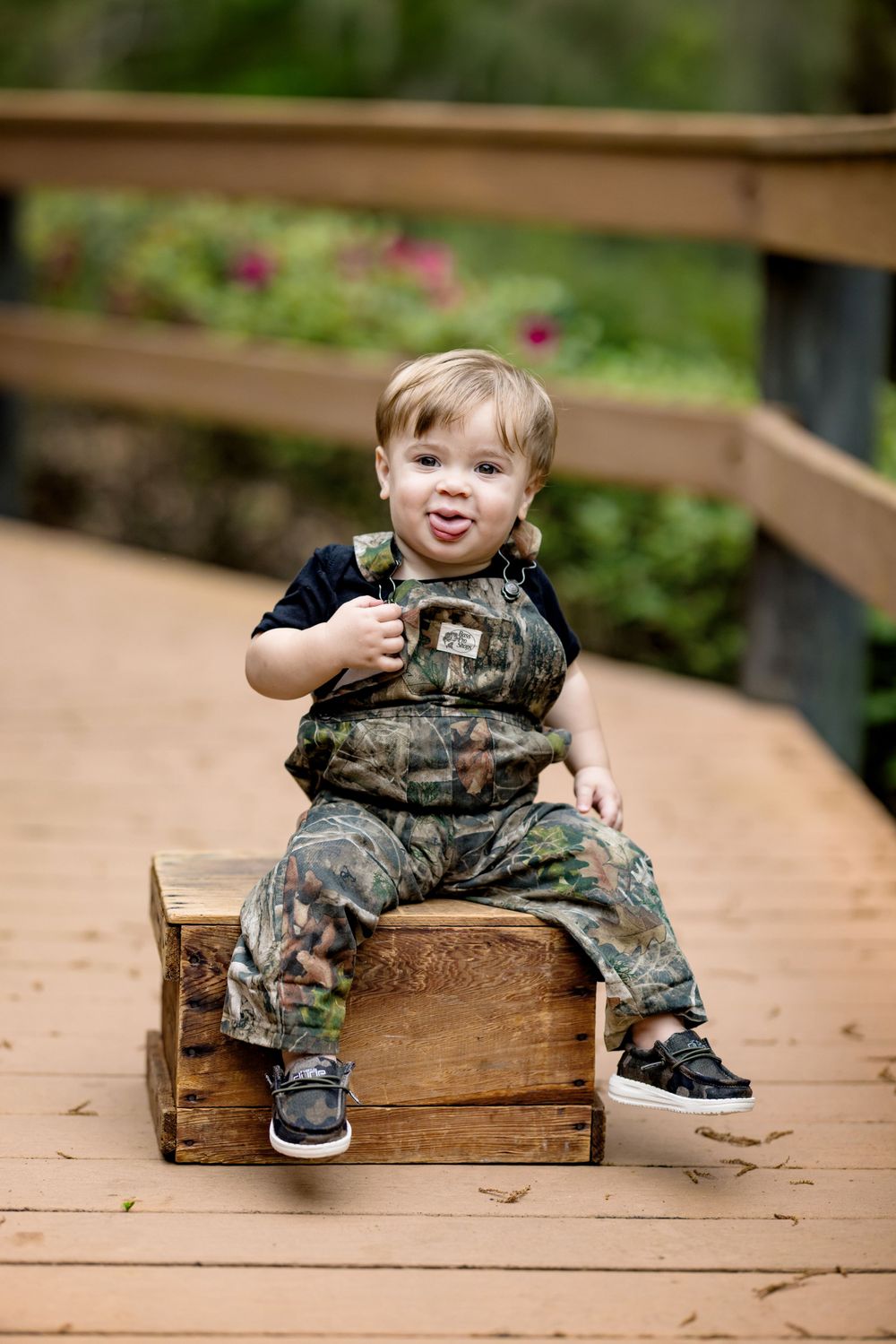 A small figure in camouflage overalls sits on a wooden crate outdoors.