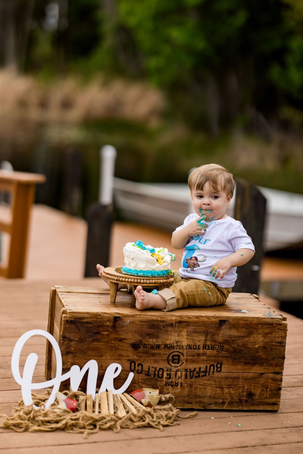 First birthday cake smash session on rustic wooden crate with 'ONE' sign on deck.