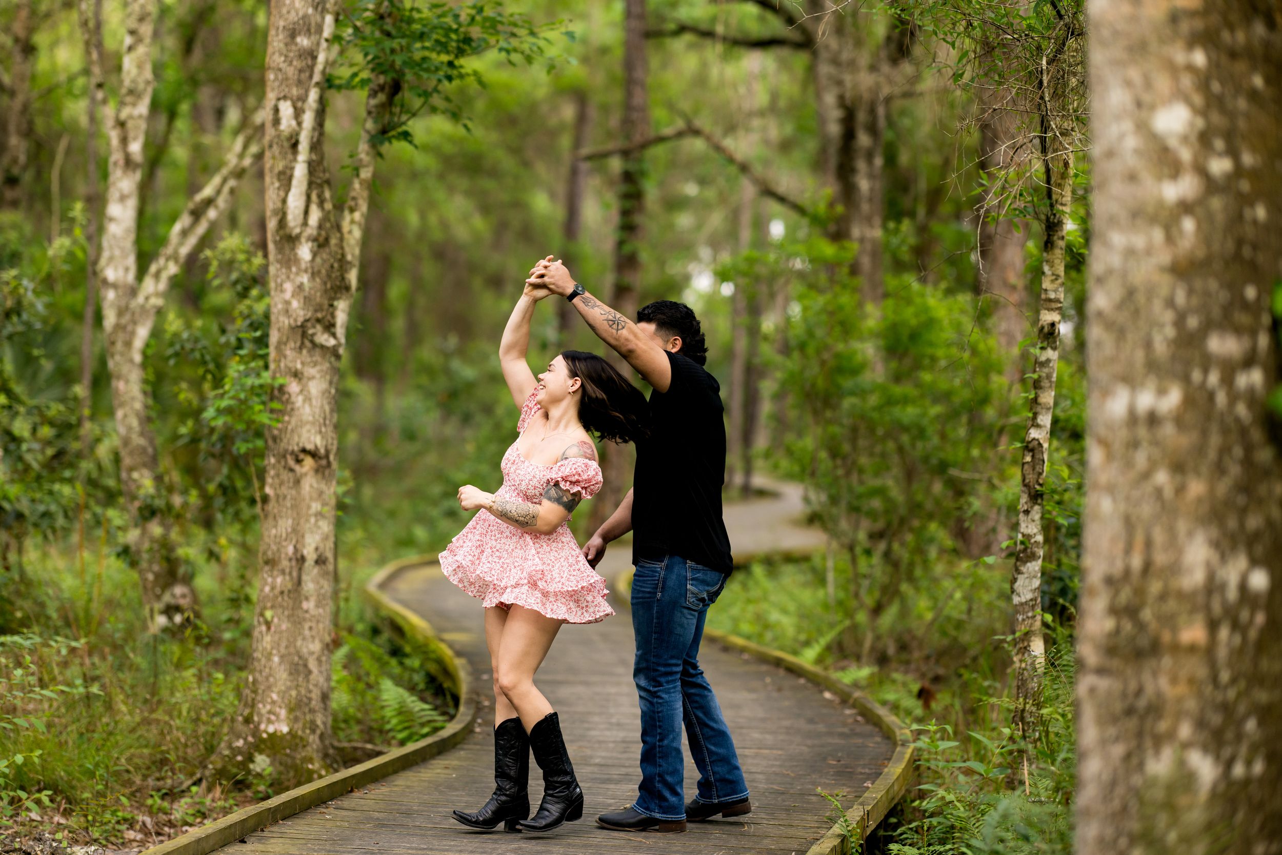 Couple dancing together on a wooden boardwalk surrounded by forest greenery.