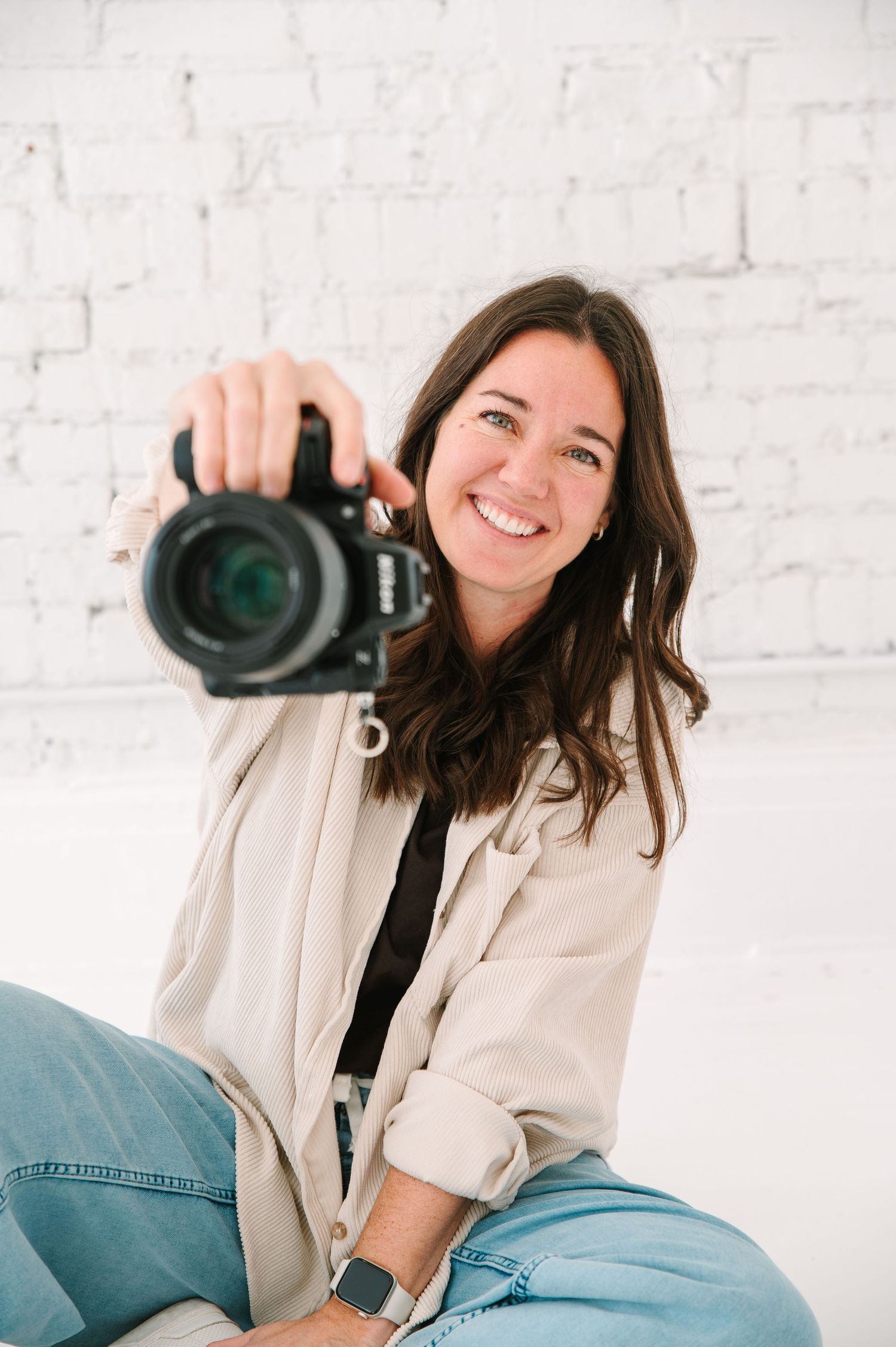 Black and white portrait of photographer with camera against plain wall.