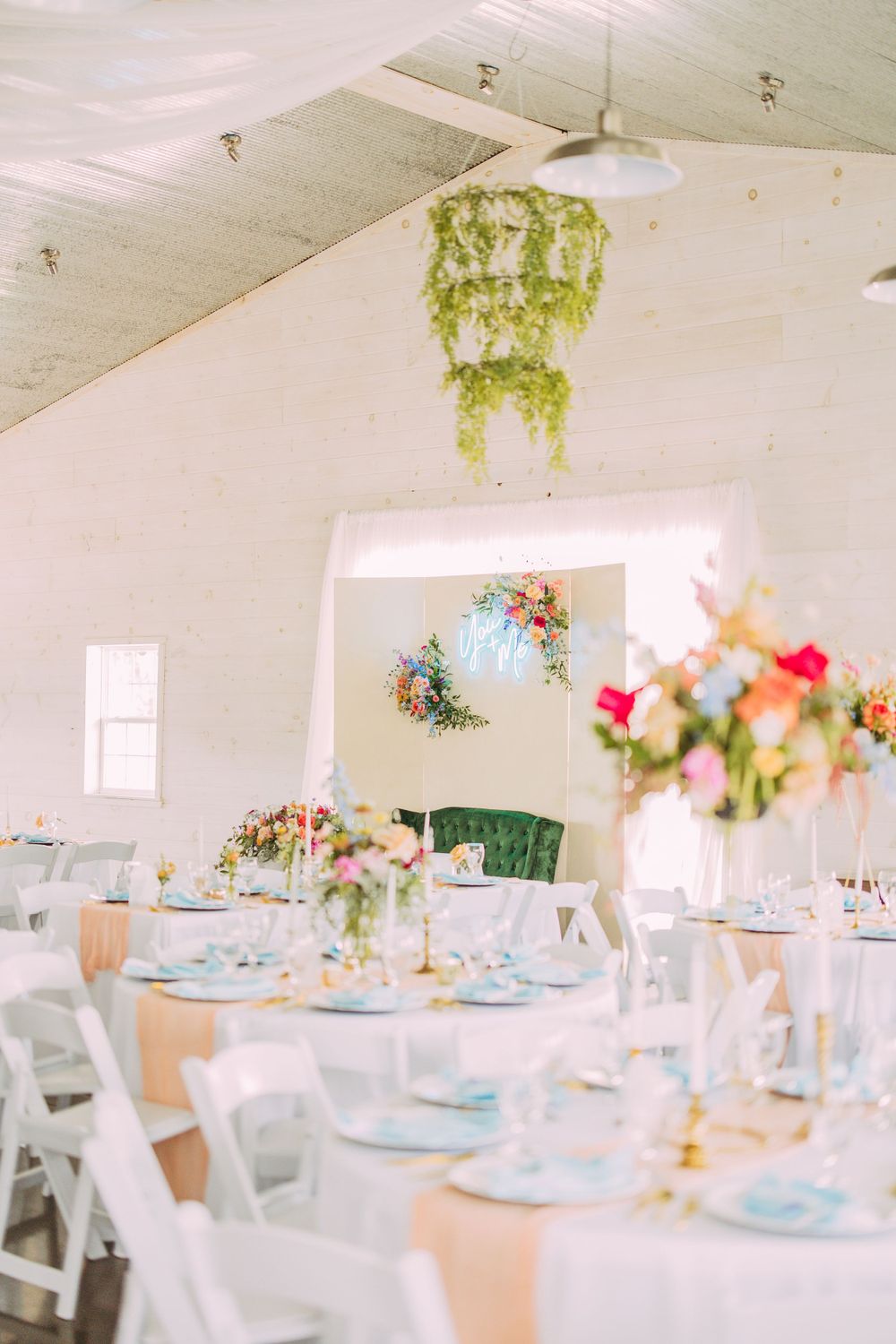 Elegant wedding reception setup with white chairs, pale blue accents, and hanging greenery chandelier.