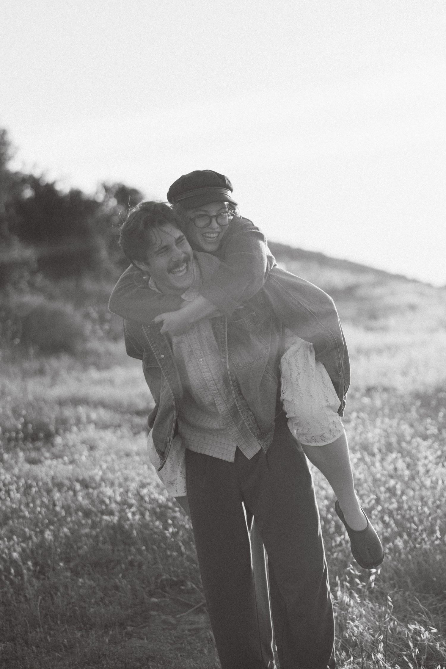 Black and white engagement photo of a bride-to-be getting a piggyback ride in the hills of Southern California