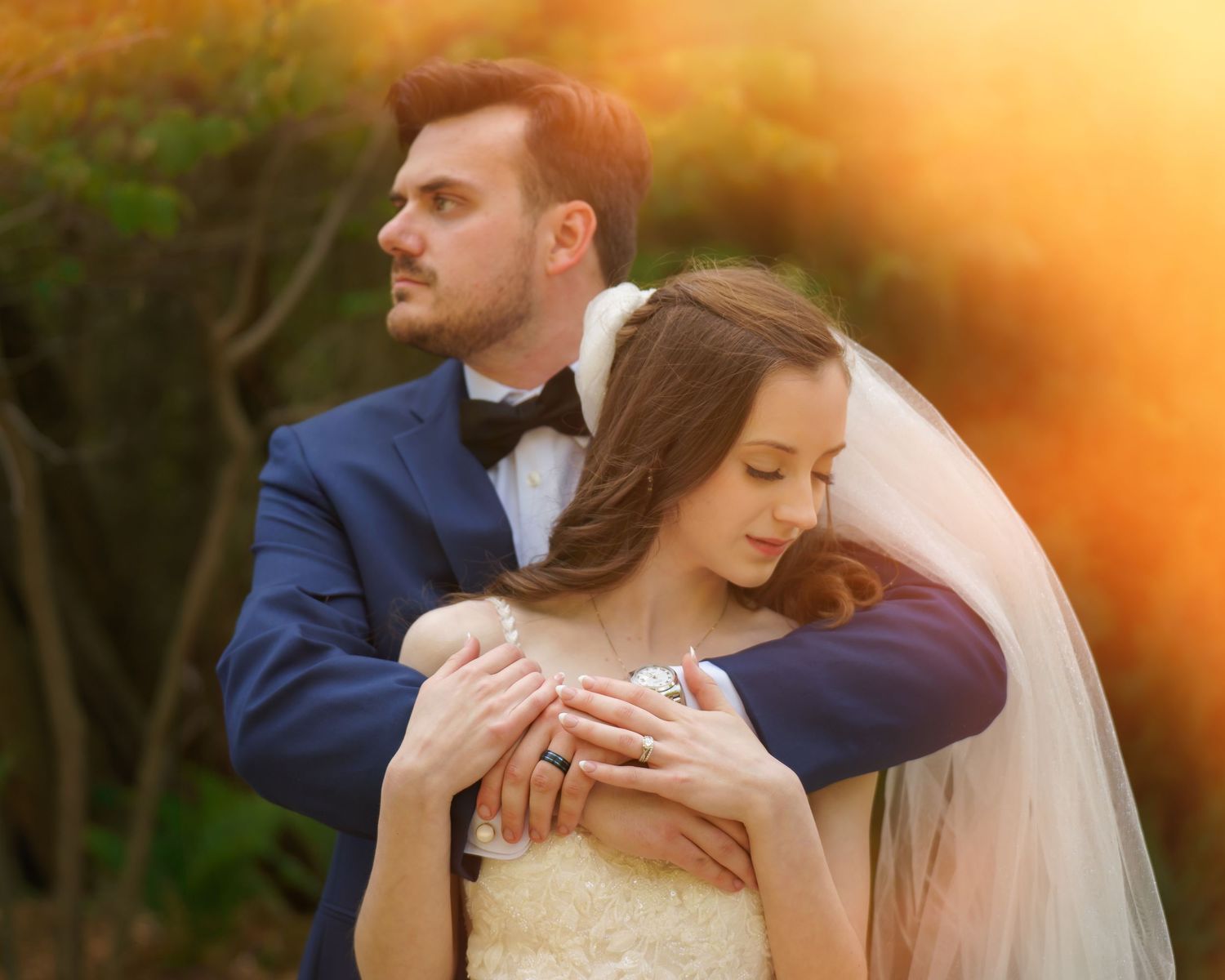 Wedding rings nestled among wheat stems and floral arrangements in beige and purple tones against a dark wooden backdrop.