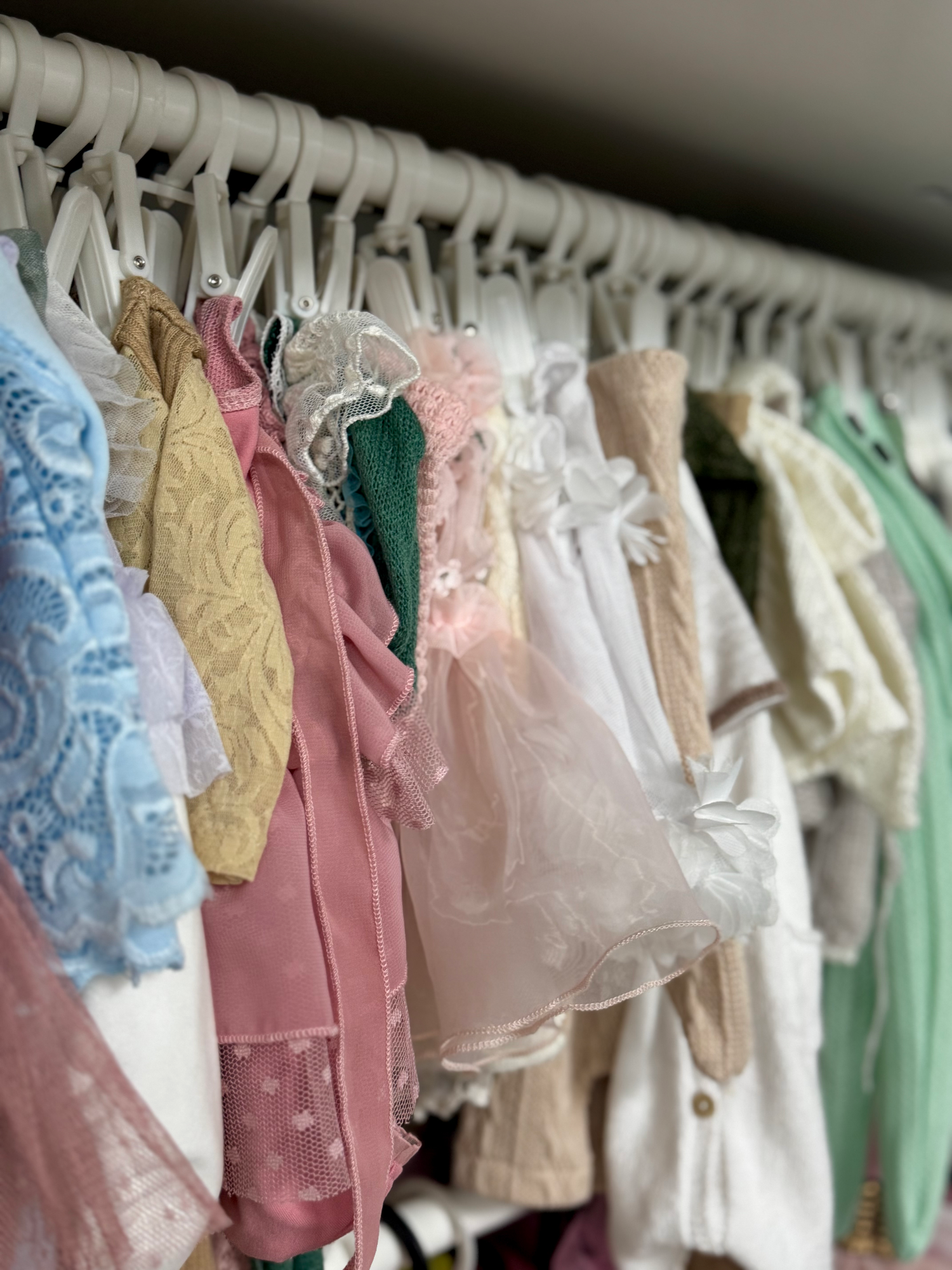 Pastel and light-colored dresses hanging on white hangers in a closet, showcasing delicate lace and soft fabrics.