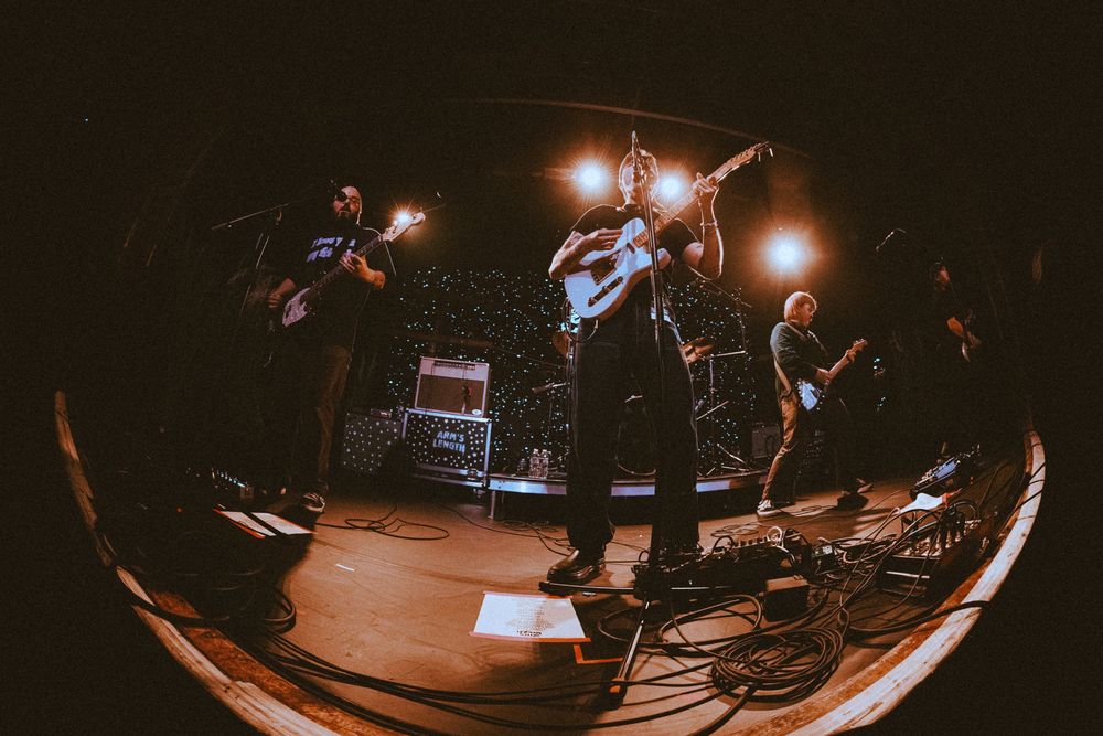Full band performs on stage with warm spotlights captured with wide fisheye lens at live concert.