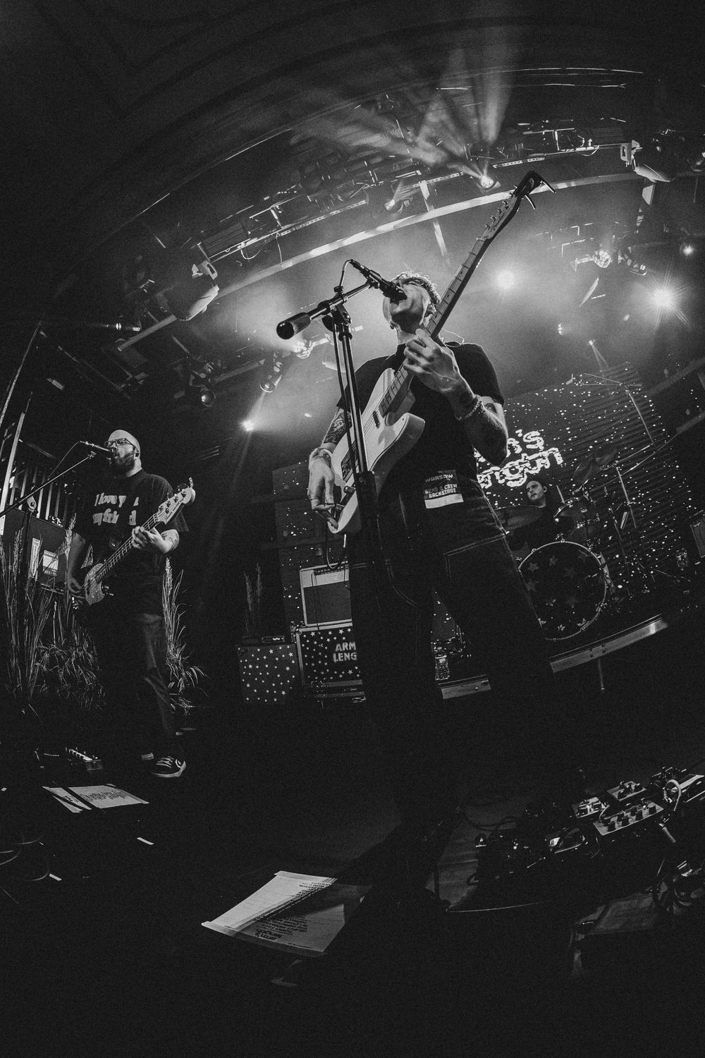Two guitarists perform on stage captured with fisheye lens at a live rock concert with bright lights.