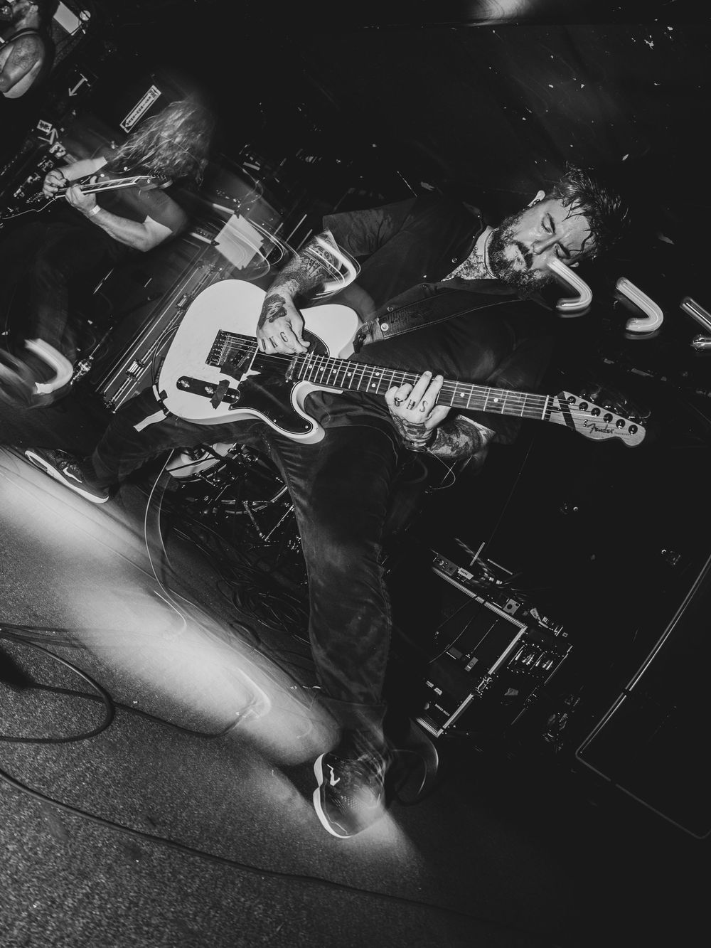 Black and white photo of guitarist playing Fender Telecaster on stage during live rock concert performance.