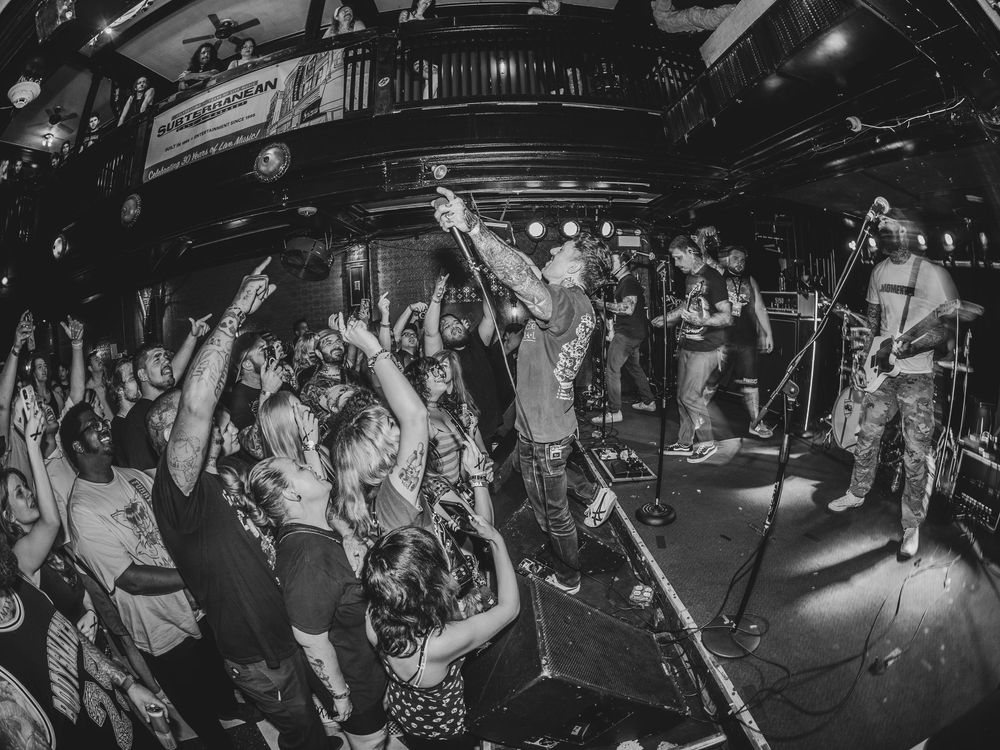 Black and white photo of a lively punk rock concert with crowd dancing and band performing on stage.