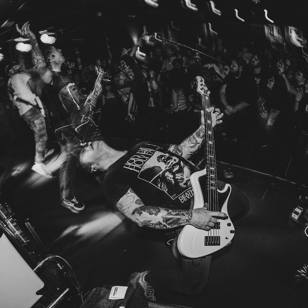 Tattooed guitarist performs energetically on stage at a packed punk rock concert in black and white photo.