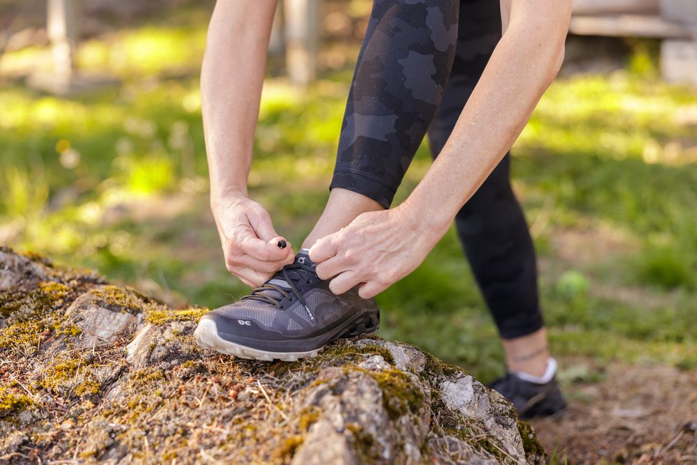 woman health coach tying running shoes foot propped up on rock for lifestyle branding stock photo in Seattle, WA