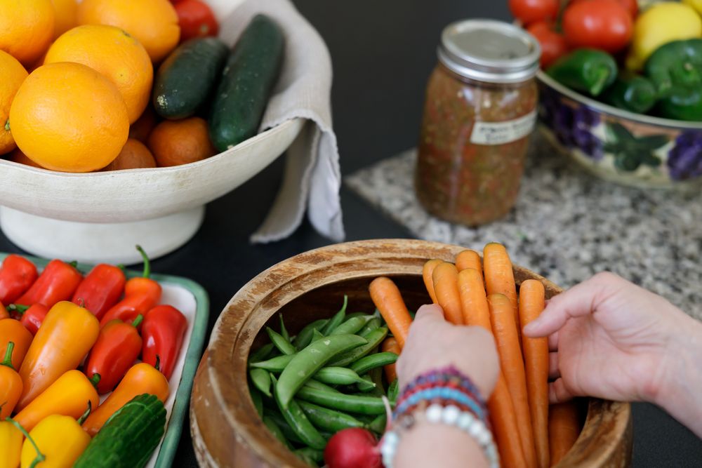 woman hands placing bunch of washed carrots into bowl with other fresh veggies for branded stock phot in Stanwood, WA