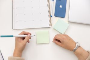 woman hands holding pen getting ready to write on Post-It Notes with calendar, phone & laptop for branded stock photo in Bellevue, wA