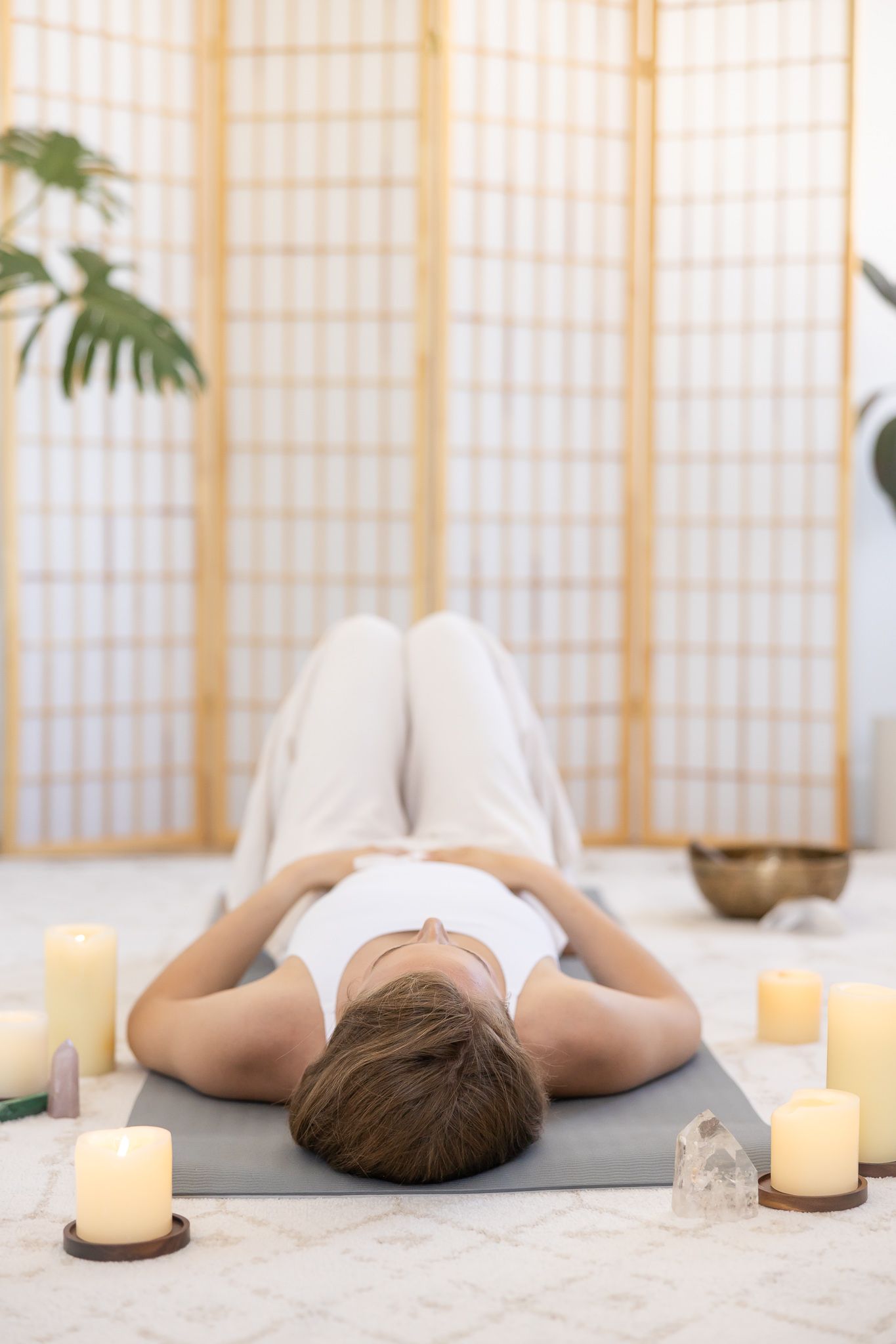 woman health coach laying on floor hands on belly, candles & crystals in soft natural light studio for branded stock photo Bellingham WA