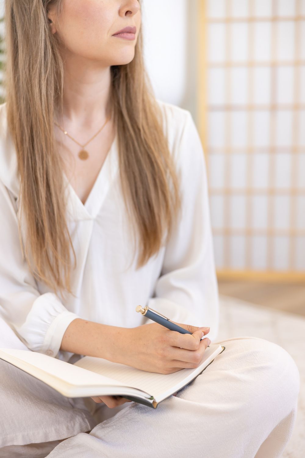 woman writing in journal looking out window, detail photo of hands soft white light for on brand stock photo for business coach in Seattle