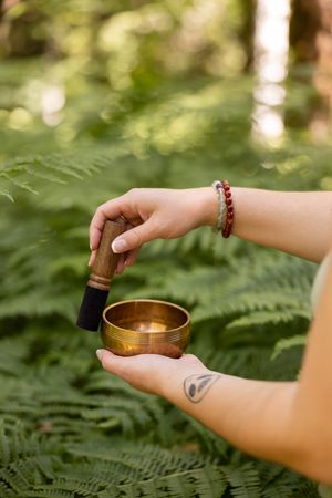 Woman spiritual energy healer playing brass sound bowl in wooded forest for lifestyle branded stock photo in Bellevue, WA