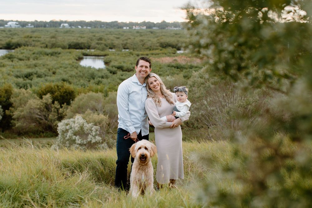 A family and their golden retriever pose together in a scenic natural setting.