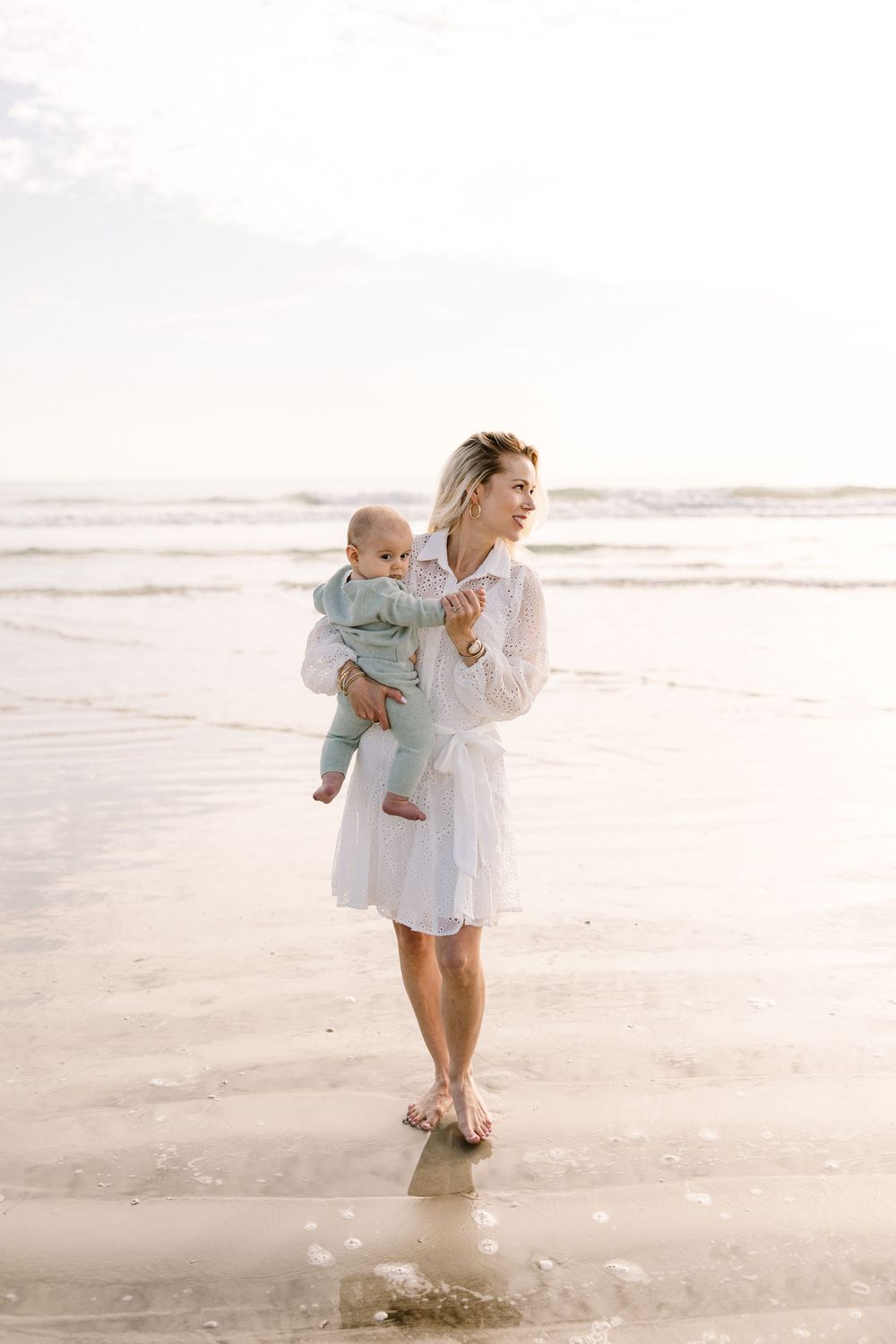 A serene beach scene with parent and baby in matching white outfits at sunset.