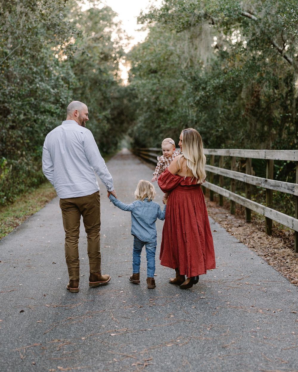 A family takes an evening stroll together on a tree-lined path with wooden railings.