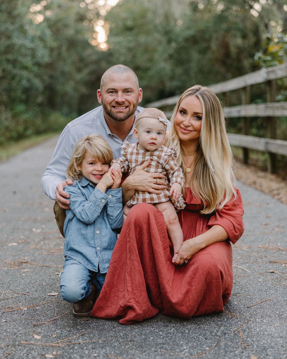 A family portrait on a scenic path surrounded by trees and wooden fencing.