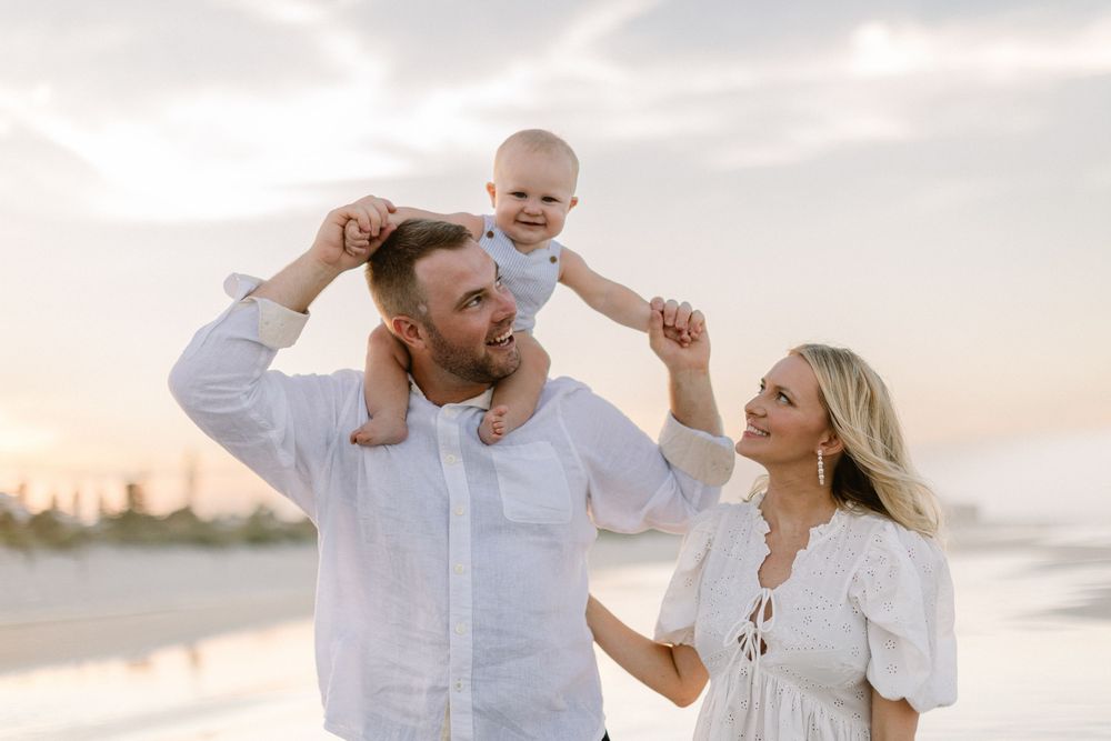 A group in white outfits shares joyful moments during a sunset beach photoshoot.