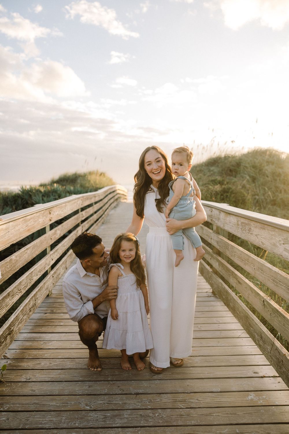 Family enjoying a tender moment together on a wooden boardwalk at sunset by the beach.