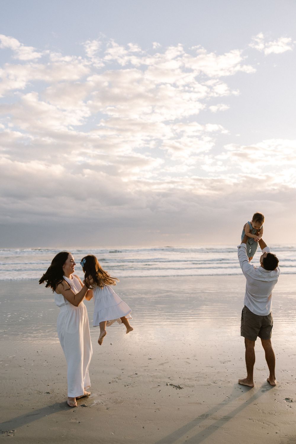Family enjoying a sunset moment together on a beach with cloudy sky and ocean waves in the background.