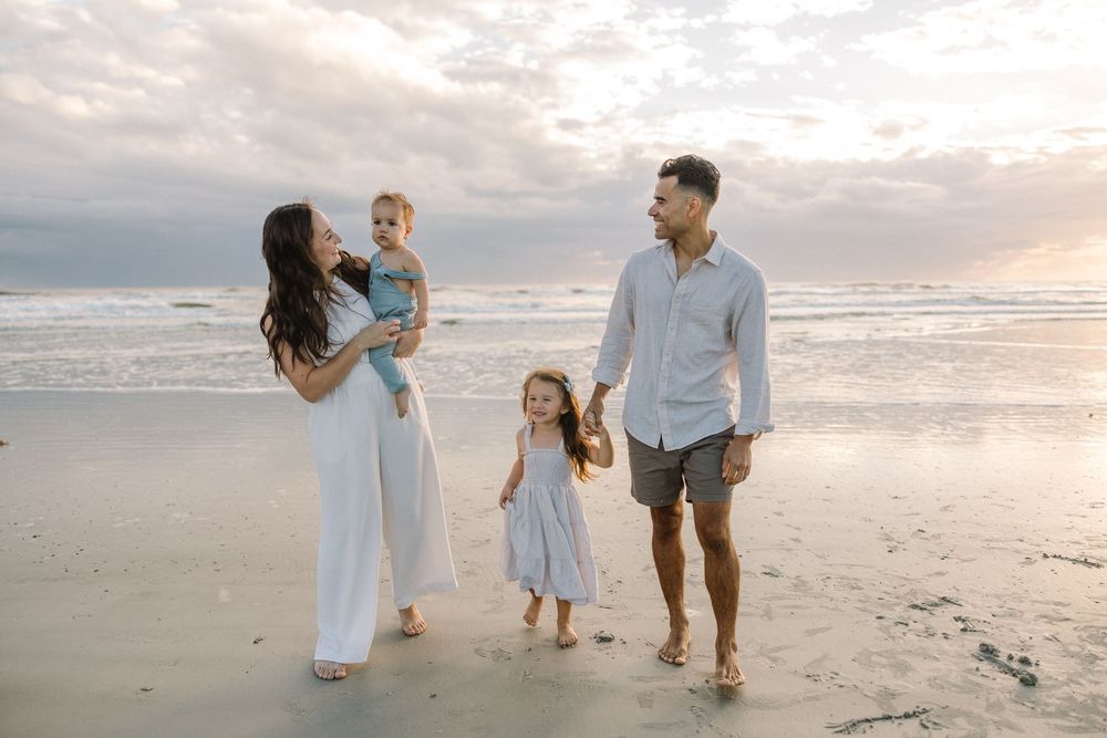 Family walking together on a sandy beach at sunset with waves rolling in the background.
