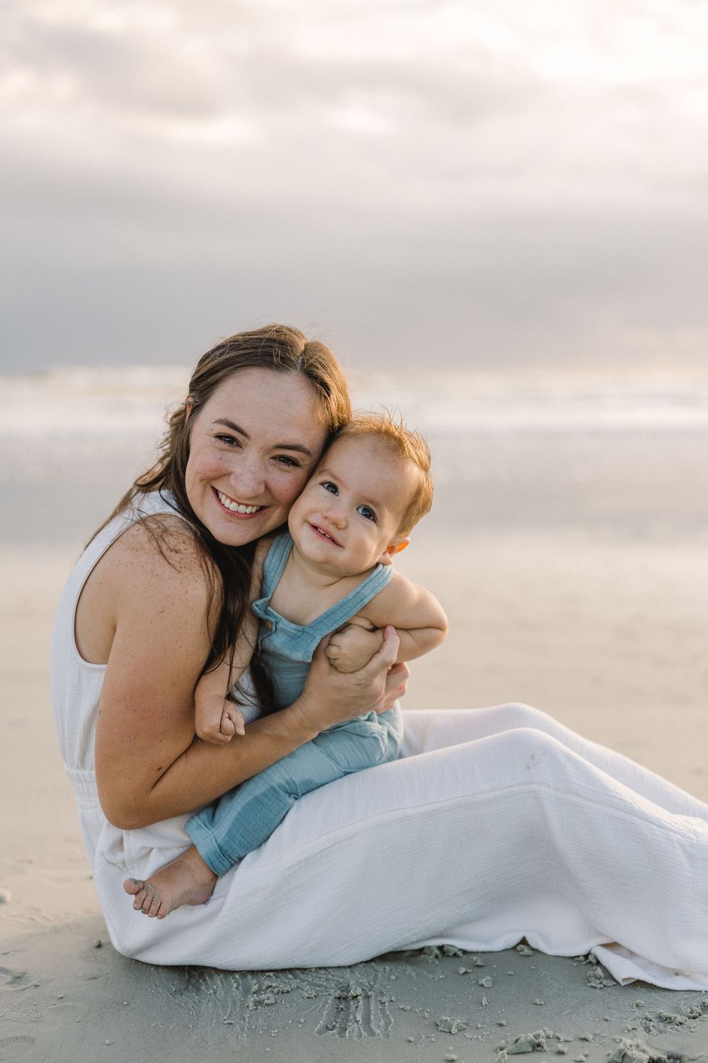 A heartwarming beach photoshoot shows tender moments between two people laying in the sand at sunset.